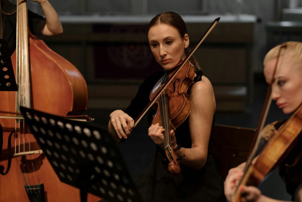 A young female violinist playing passionately in an indoor symphony concert setting.